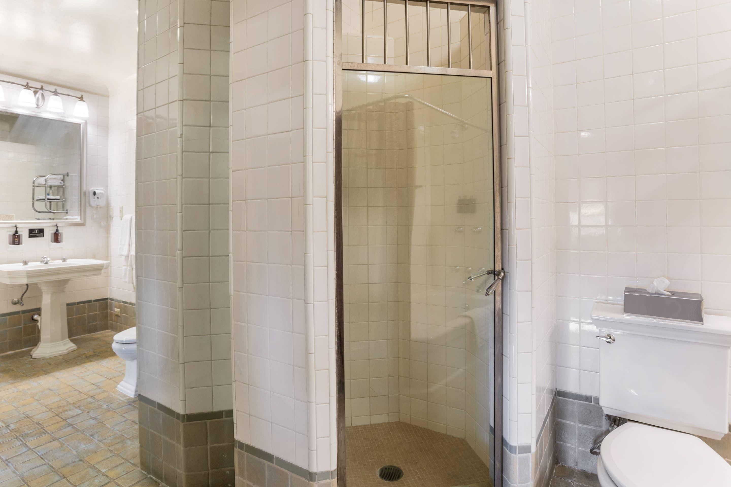Un baño con ducha de vidrio, lavamanos pedestal, inodoro y espejo.