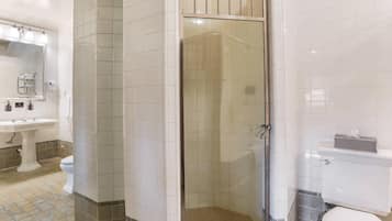 Un baño con ducha de vidrio, lavamanos pedestal, inodoro y espejo.