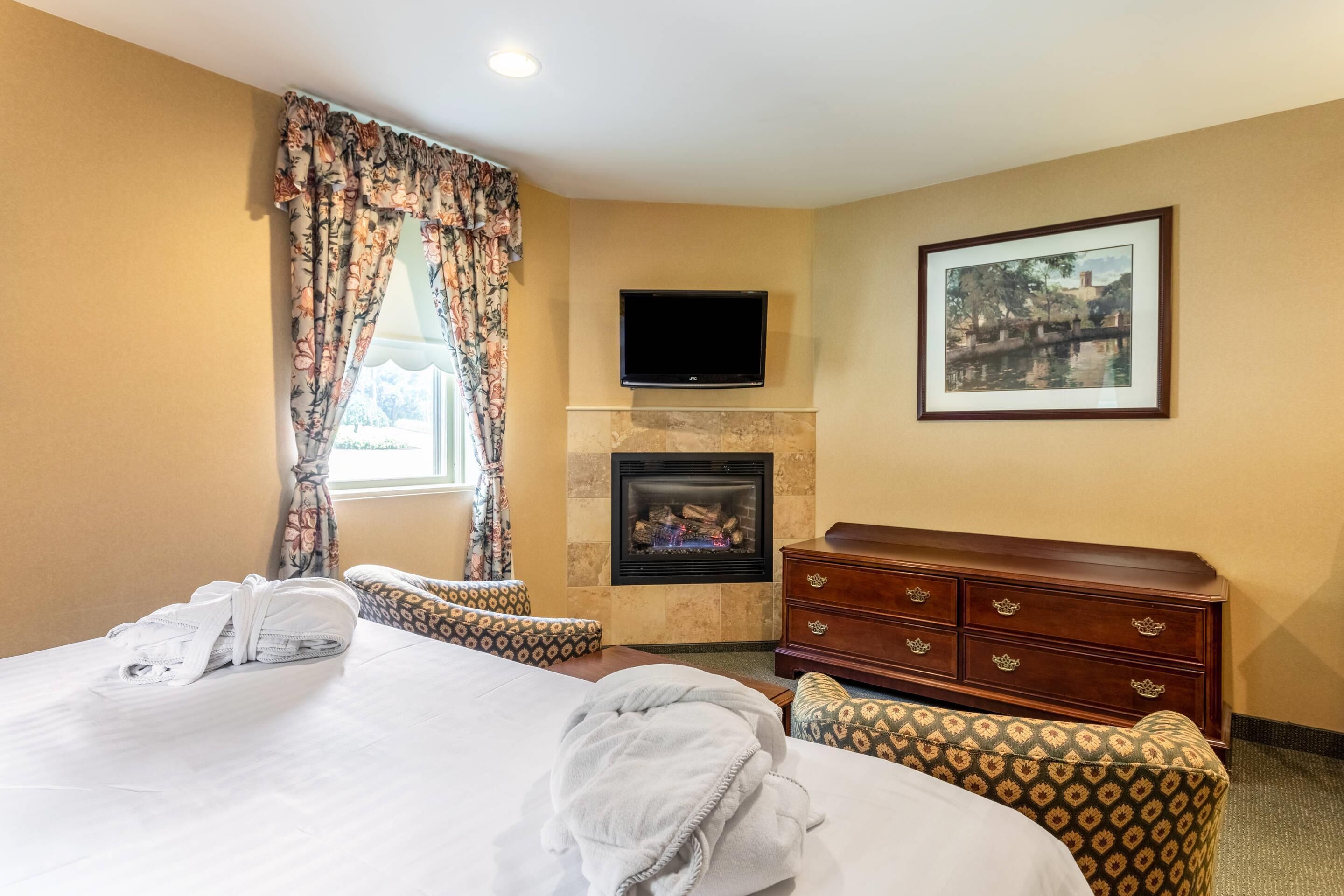 A hotel room with a bed, a fireplace, a TV, a dresser, and a framed picture on the wall.