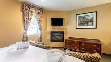 A hotel room with a bed, a fireplace, a TV, a dresser, and a framed picture on the wall.
