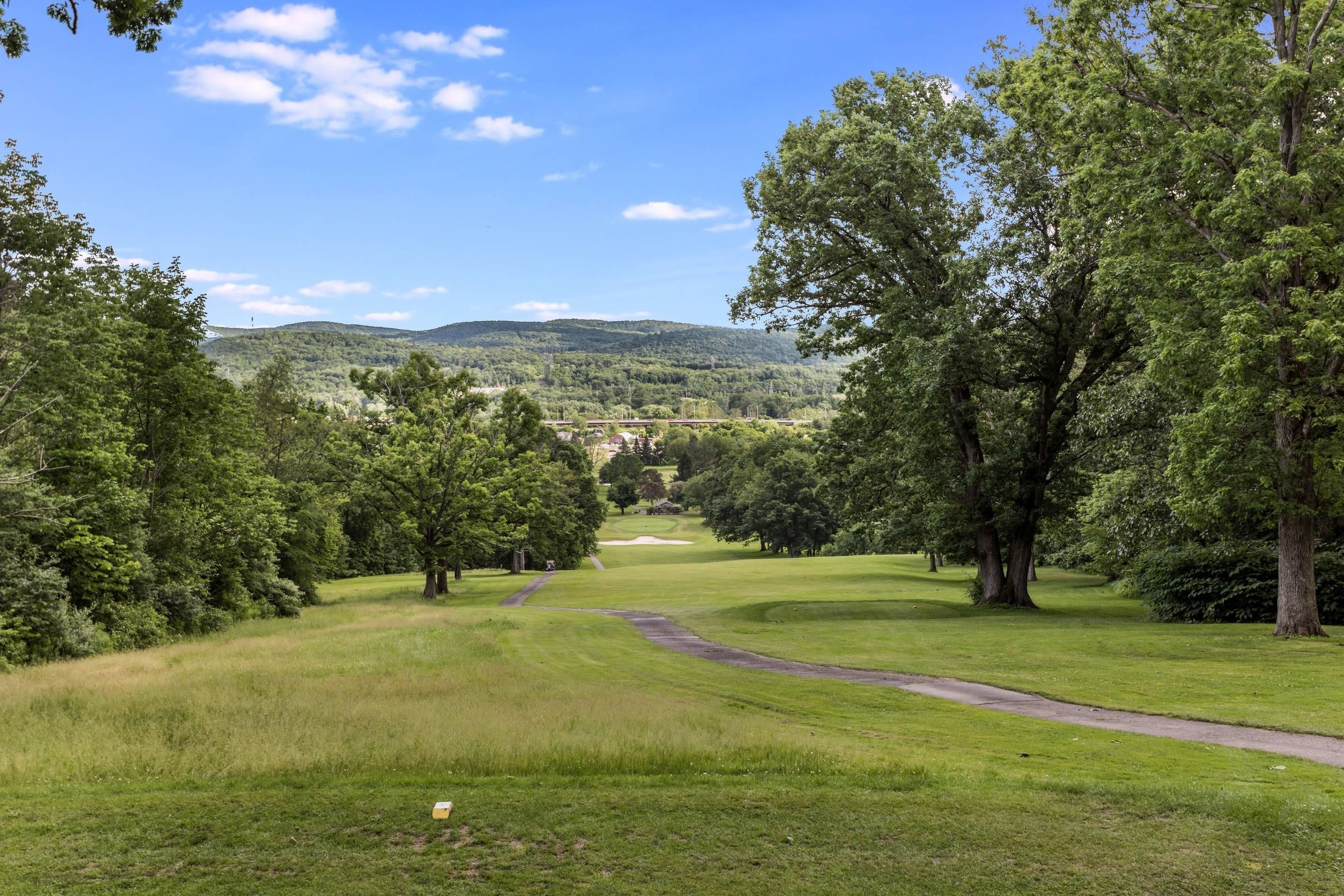 Un campo de golf con un camino despejado que conduce a un edificio distante, rodeado de abundante vegetación y árboles.