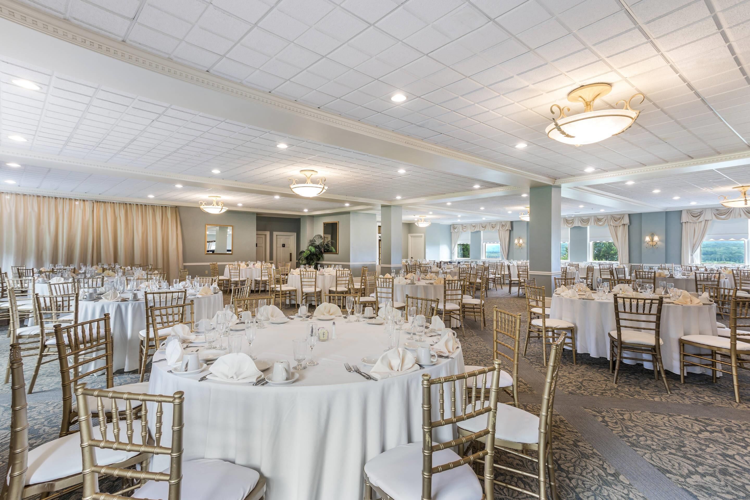 A banquet hall with round tables, gold chairs, and white tablecloths.