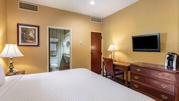 A hotel room with a bed, two bedside lamps, a television, a dresser, and a door leading to a bathroom.