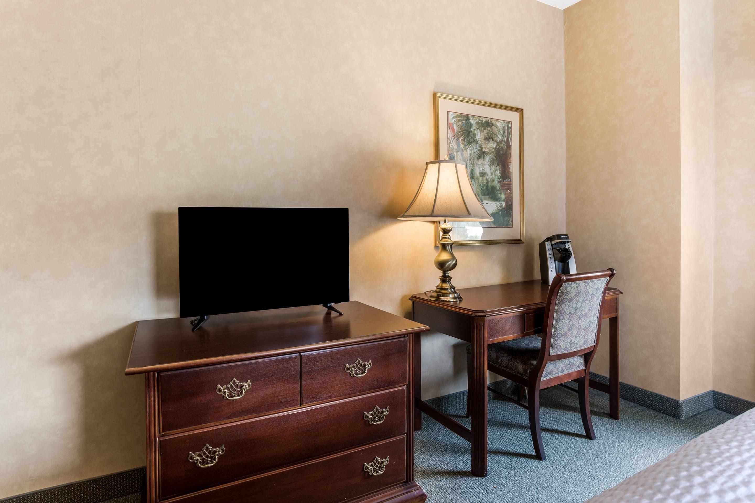 Una habitación de hotel con un escritorio de madera, un televisor, una lámpara y una silla.