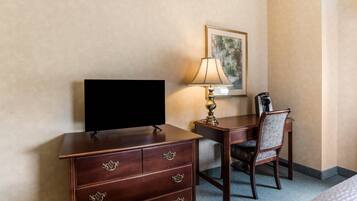 Una habitación de hotel con un escritorio de madera, un televisor, una lámpara y una silla.