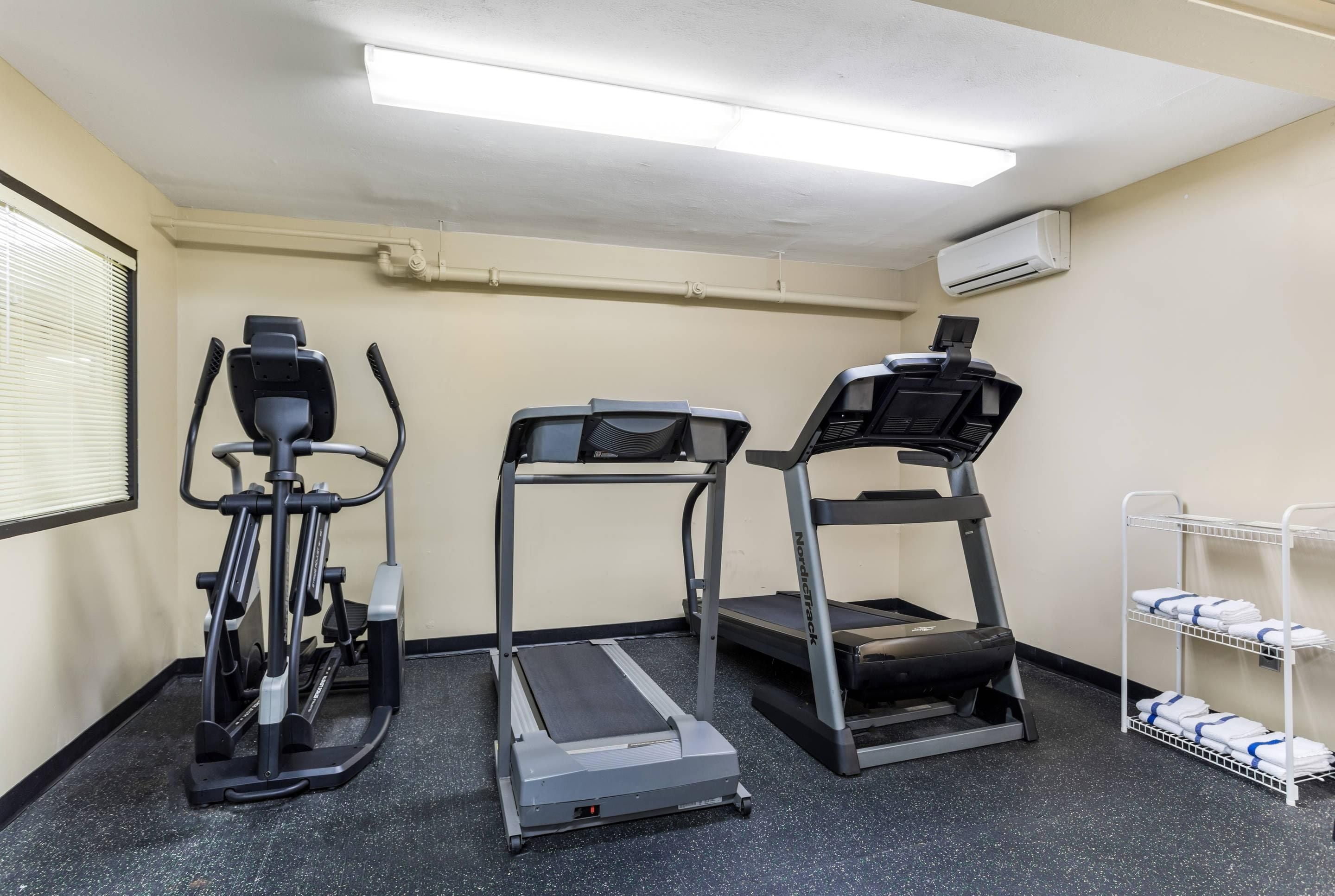 A fitness room with treadmills, an elliptical, and a rack of towels.
