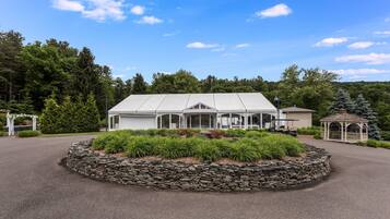 A large, modern building with a covered patio area, surrounded by a stone retaining wall and lush greenery.
