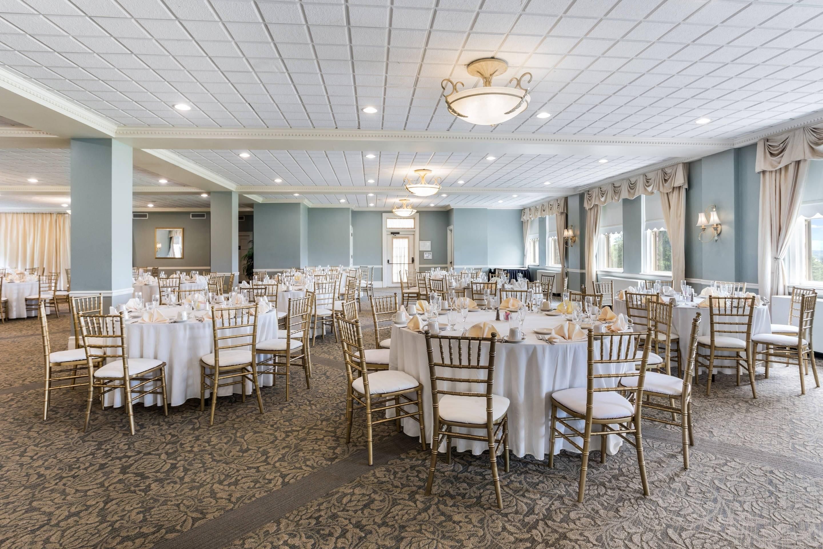 A large banquet hall with round tables, gold chairs, and a patterned carpet.