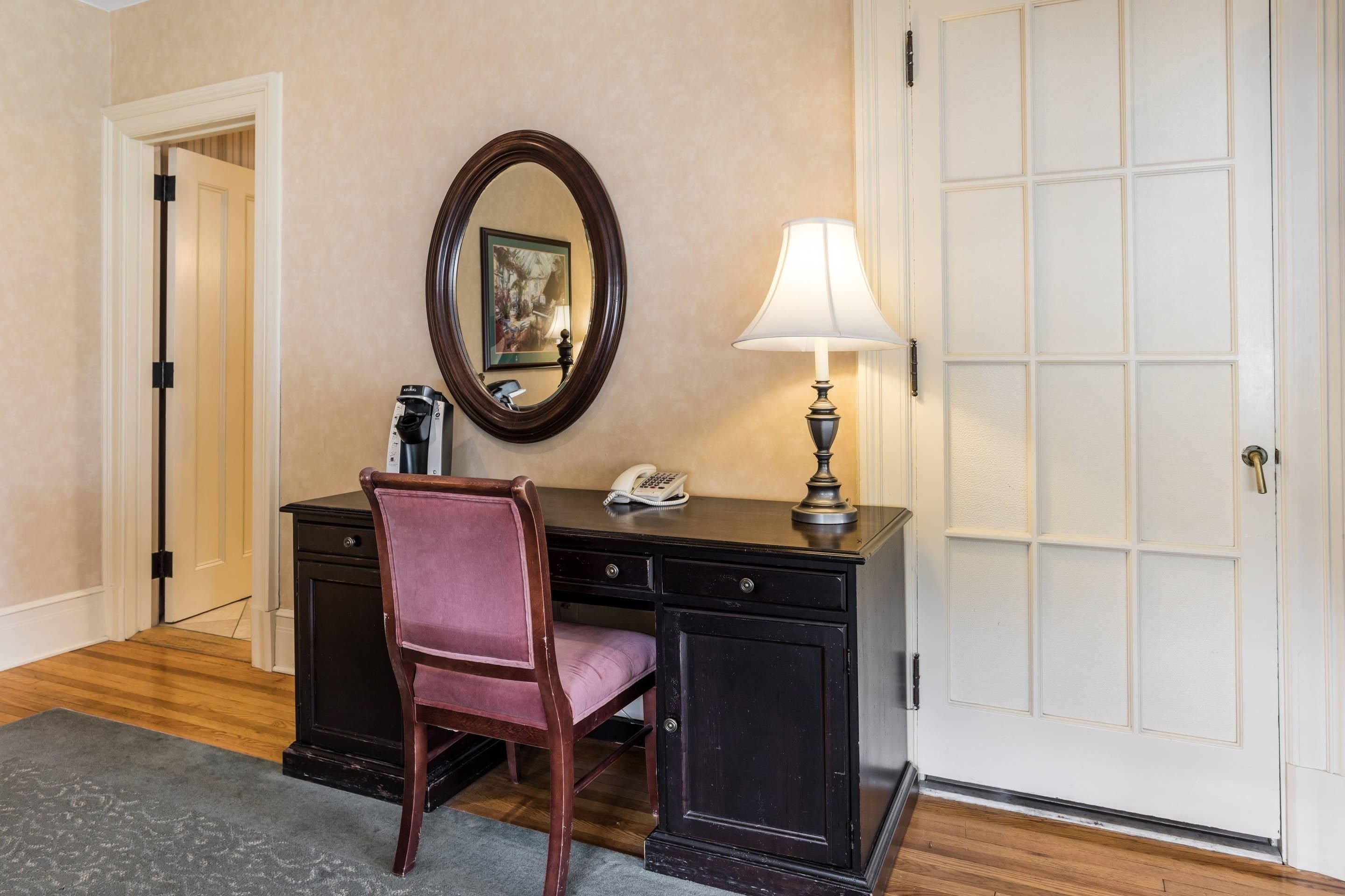 A room with a desk, chair, lamp, and a large mirror.