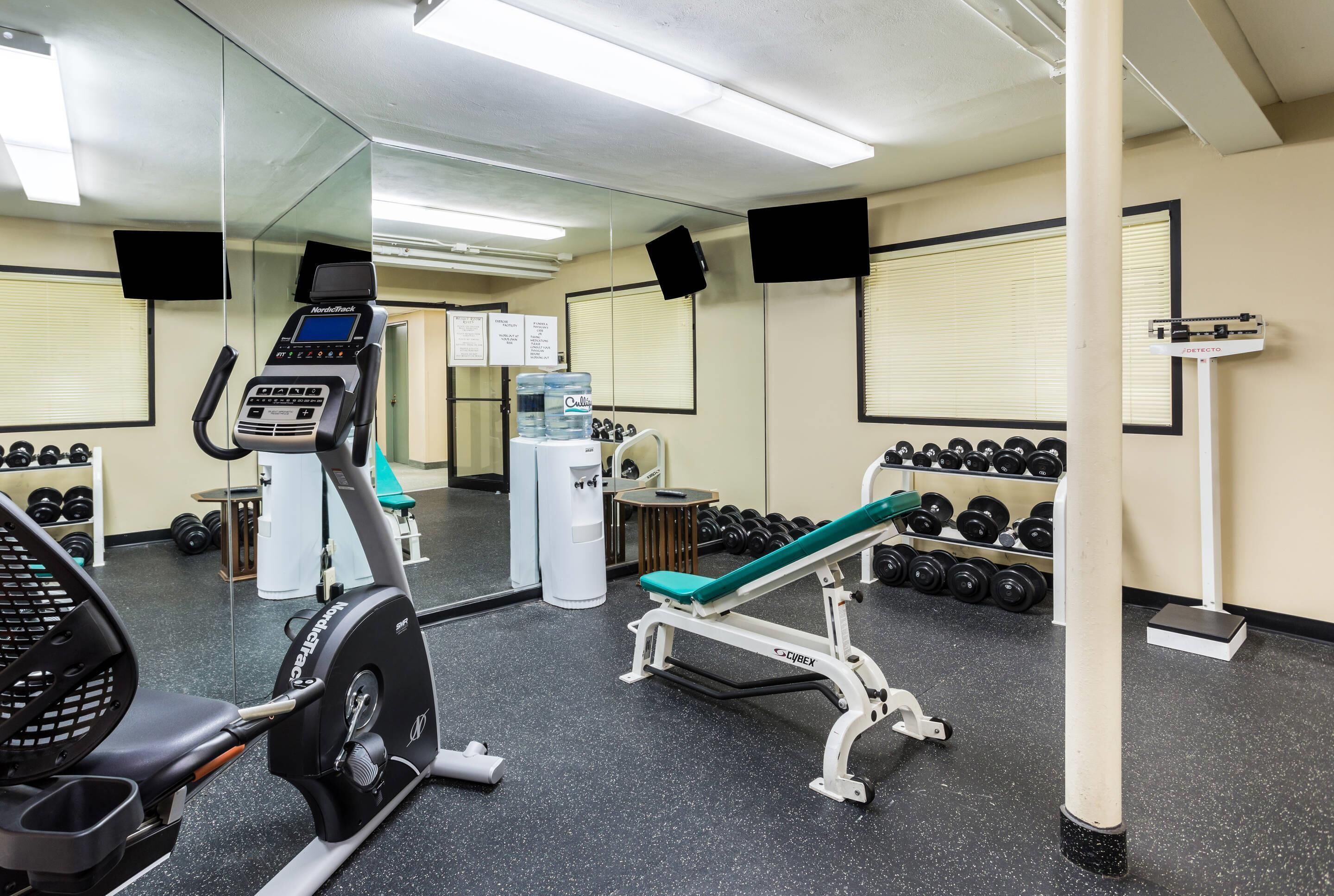 A gym with cardio equipment, weightlifting stations, and a bench.