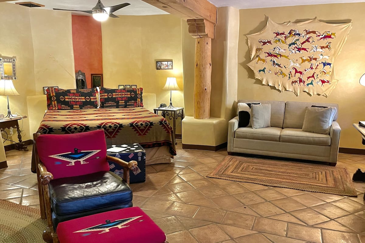 Una habitación con una cama, un sofá, una silla, un tapete y una pared con una pintura tribal.