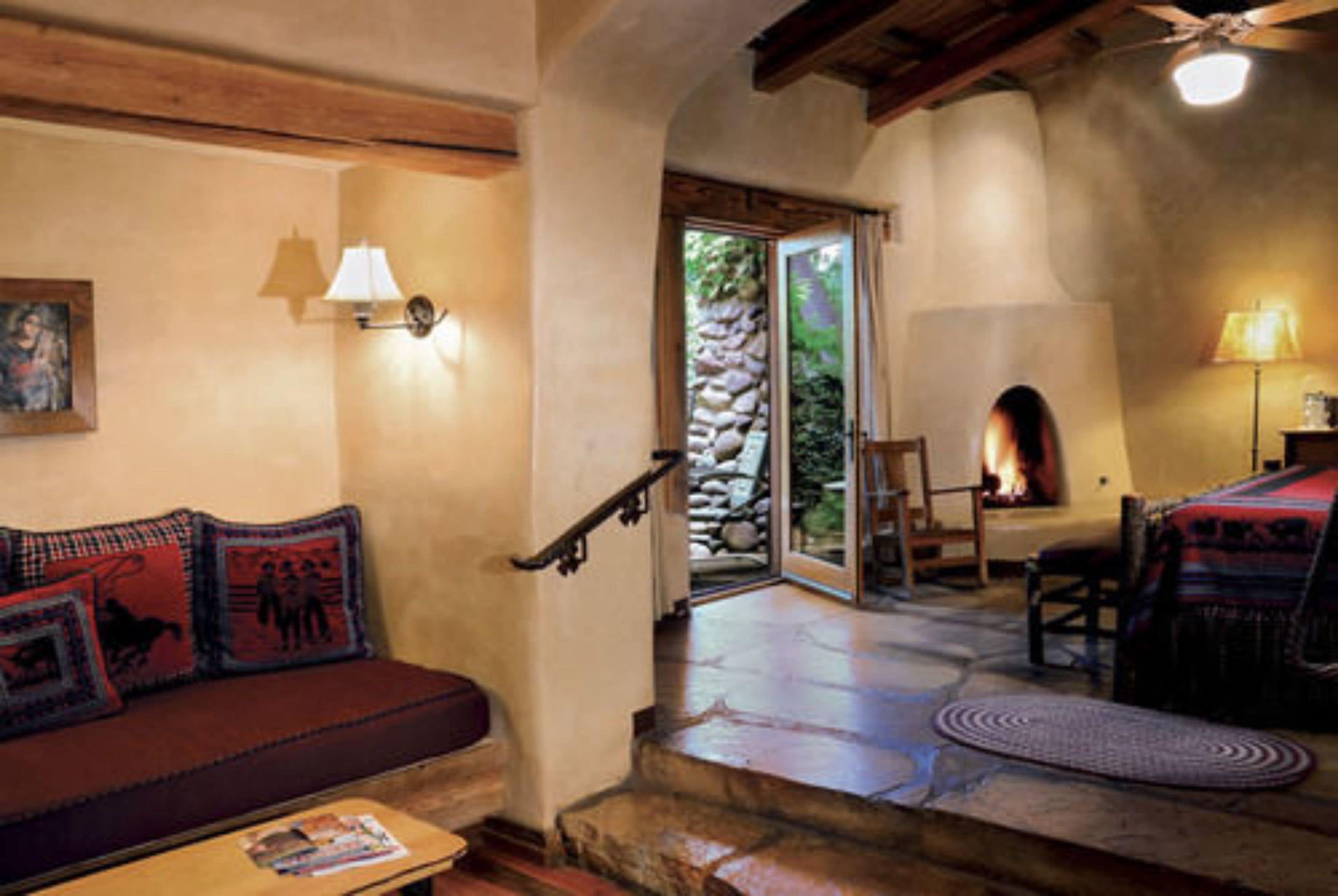Un interior acogedor con una chimenea de piedra, una escalera de madera y un sofá rojo con cojines estampados.