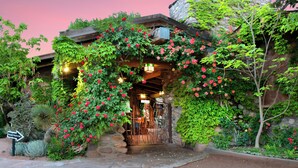 A rustic building with a stone facade, a wooden archway covered in red flowers, and a sign indicating a registration area.
