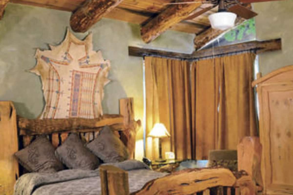 Una habitación rústica con una cama de madera, un ventilador de techo y un tapiz grande en la pared.