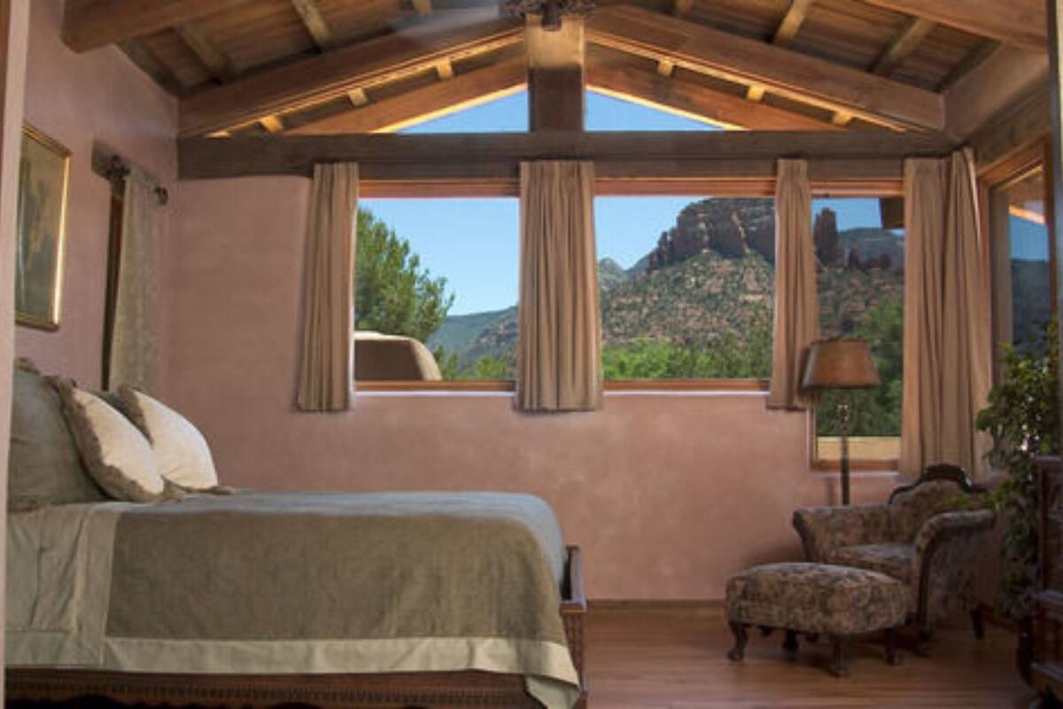 Un dormitorio con una cama grande, una silla, un escritorio y vistas a las montañas.