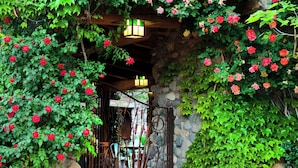 A rustic stone building with a wooden archway covered in red roses.