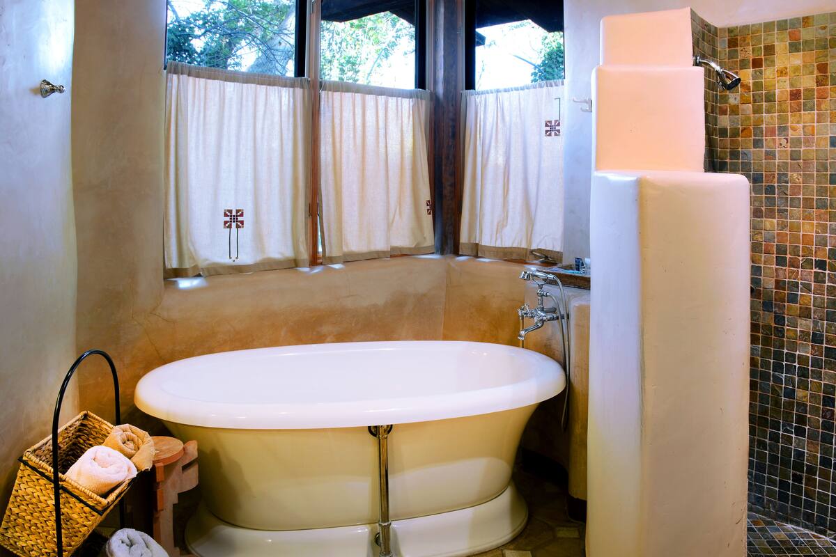 Un baño con una bañera independiente, zona de ducha y una ventana con cortinas.