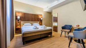Una habitación de hotel moderna con una cama grande, lámparas de noche, una mesita con sillas y un espejo en la pared.