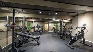 Ett gym med olika typer av träningsutrustning, inklusive en bänkpress, hantlar och konditionsmaskiner.