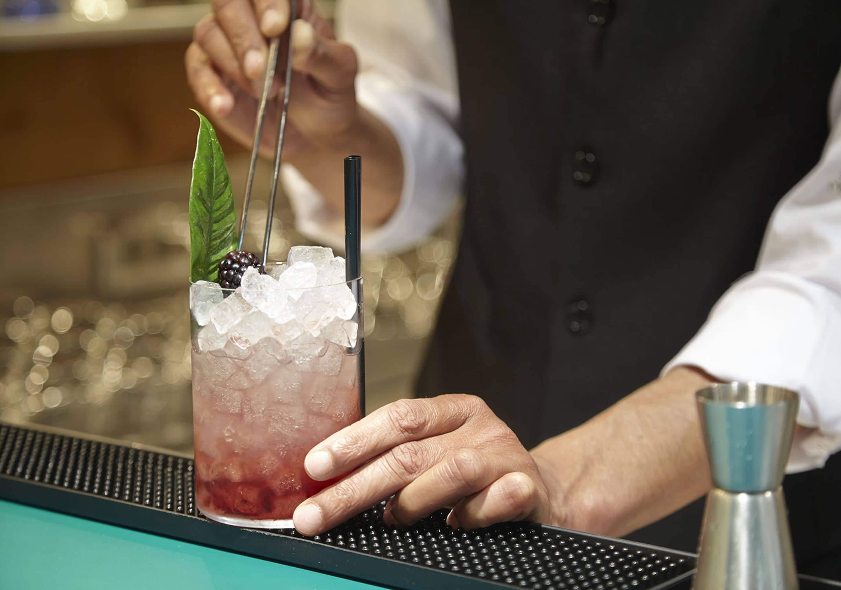 A bartender preparing a drink with a lime wedge, blackberries, and a straw.