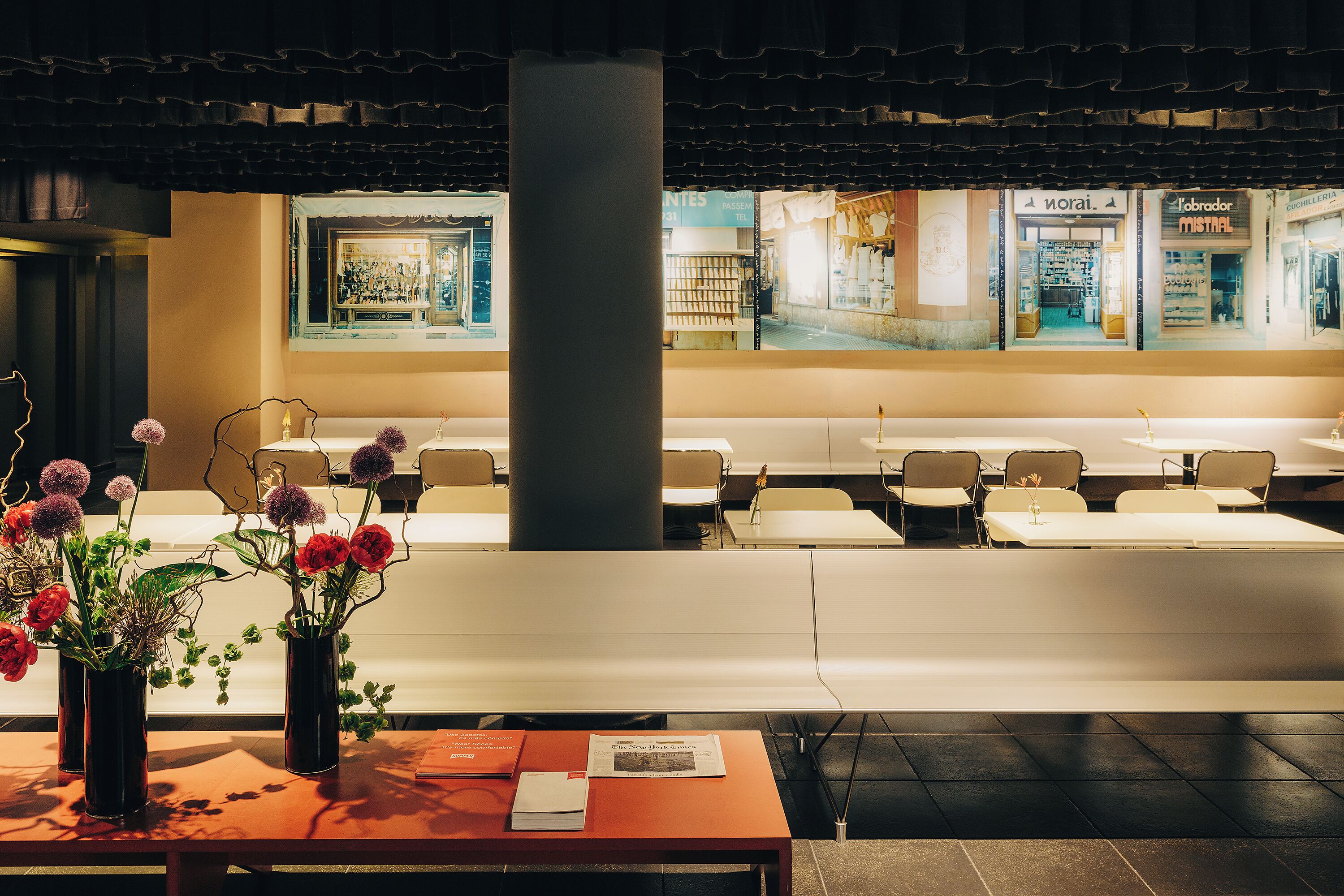 A hotel lobby with a reception desk, seating area, and a large window displaying shops.