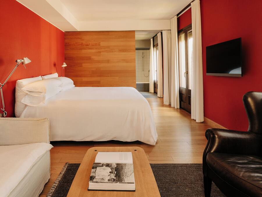 Une chambre d’hôtel avec un lit, un canapé, un fauteuil en cuir, un téléviseur à écran plat et un plancher en bois.