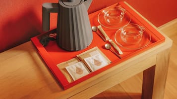 A tray with a coffee maker, teacups, and breakfast items on a wooden table against a red wall.