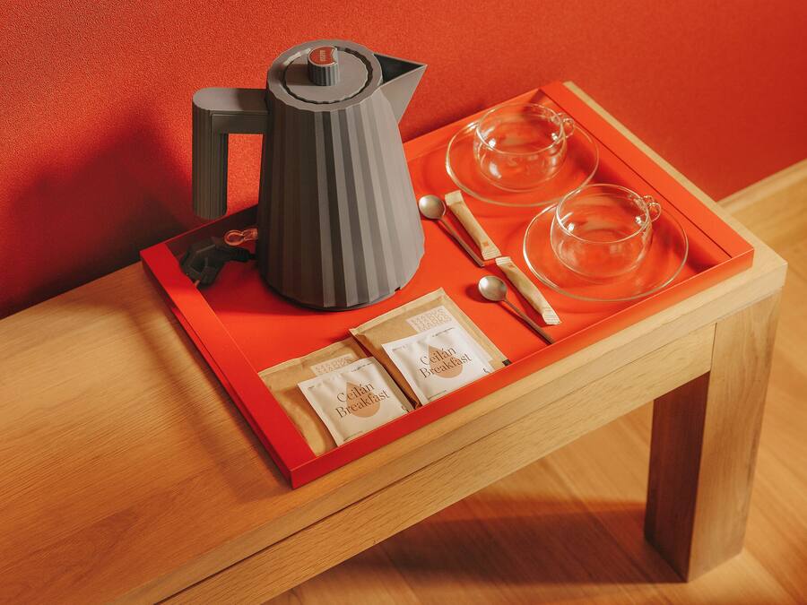 A tray with a coffee maker, teacups, and breakfast items on a wooden table against a red wall.