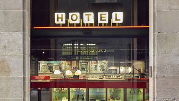 A hotel entrance with a large illuminated sign reading "HOTEL" above the door. Inside, there are glass display cases with various items on shelves.