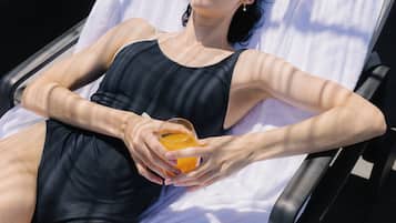 A person lying on a sun lounger with a towel, holding a glass of orange juice.