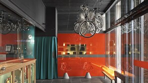 Un interno moderno con biciclette appese al soffitto, una vetrina che espone diversi oggetti e un'area salotto con una panca e due sedie dalle forme geometriche.