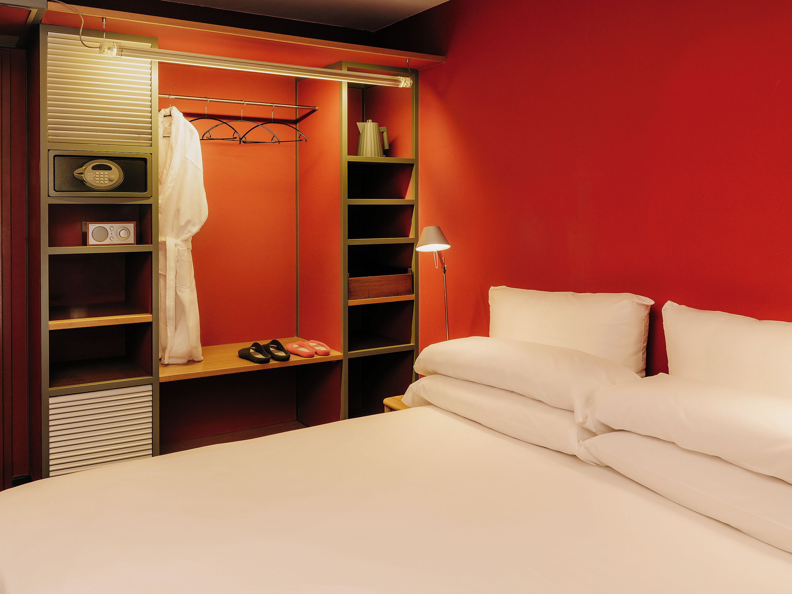 A hotel room with a bed, a closet with shelves, a lamp, and a radio.