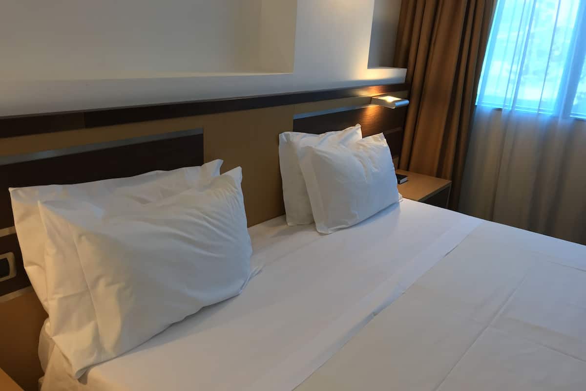 A hotel room with a neatly made bed, a nightstand, and a wall-mounted light.
