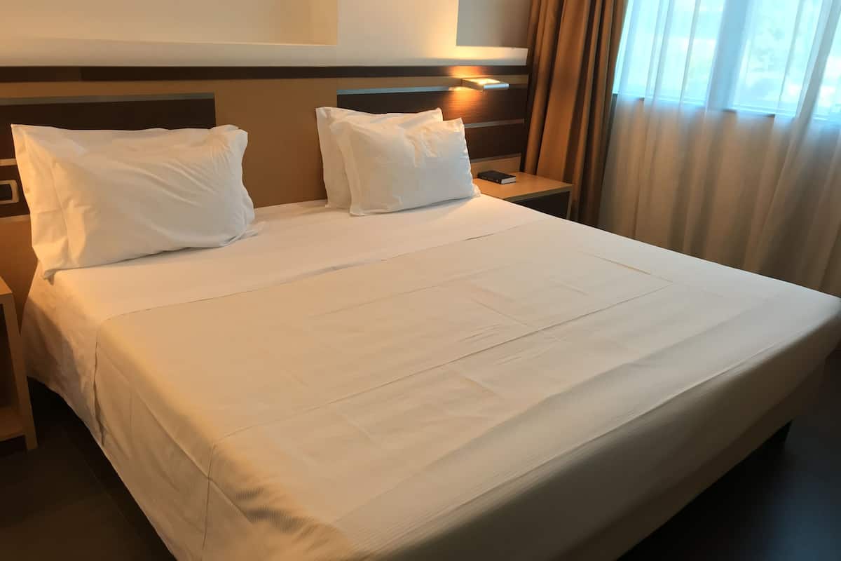 A hotel room with a large bed, two white pillows, a nightstand, and a bedside table with a book.