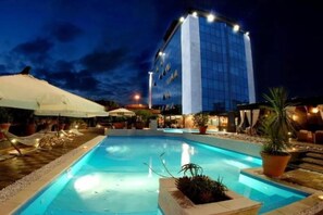 A hotel with a pool area at night, featuring a modern building with a glass facade and outdoor seating. - Bellambriana Hotel (Rome)