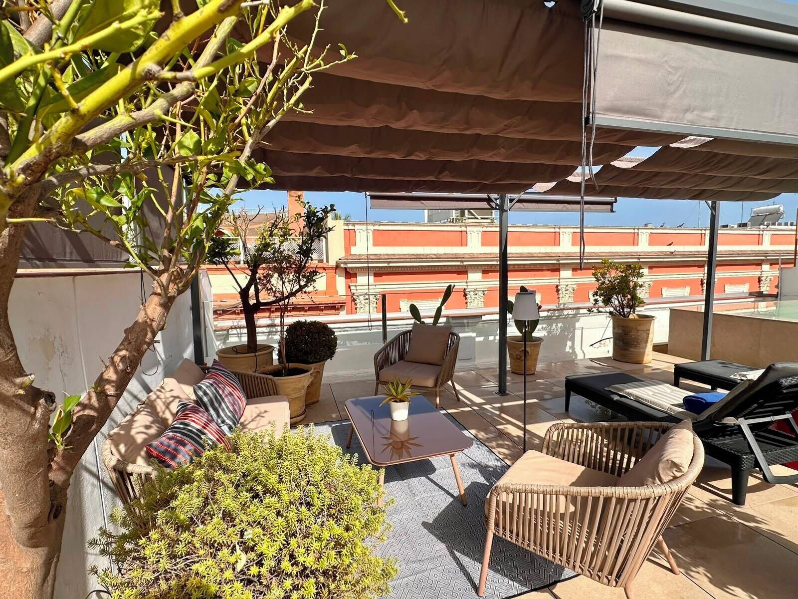 Une terrasse sur le toit, aménagée avec du mobilier d’extérieur, un pot de fleurs et offrant une vue sur les bâtiments en arrière-plan.