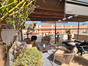 Une terrasse sur le toit, aménagée avec du mobilier d’extérieur, un pot de fleurs et offrant une vue sur les bâtiments en arrière-plan.
