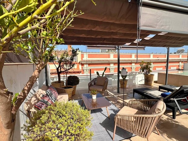 A rooftop terrace with outdoor furniture, a potted plant, and a view of buildings in the background. - Casa Romana Hotel Boutique (Seville)
