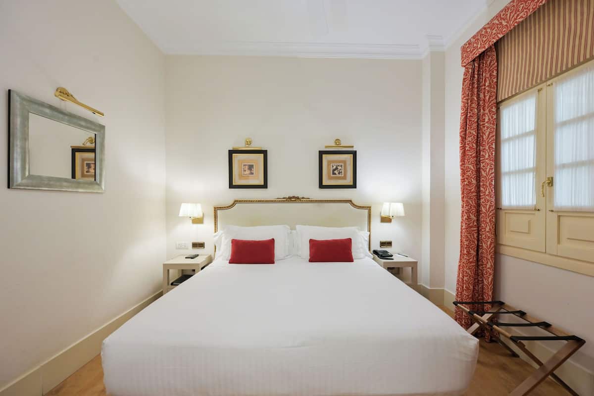 Een hotelkamer met een groot bed, twee nachtkastjes met lampen, een spiegel en ingelijste foto's aan de muur.