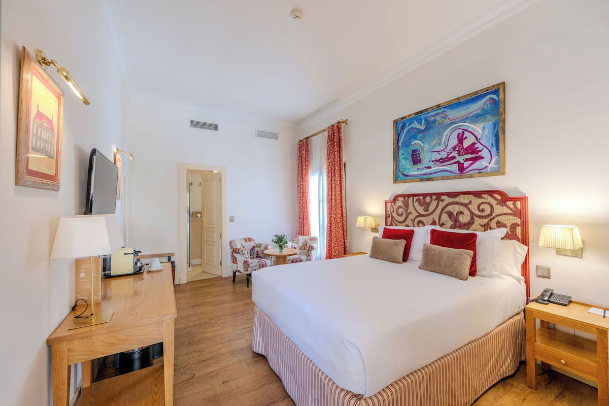 Een hotelkamer met een groot bed, een bureau, een stoel, een televisie en een schilderij aan de muur.