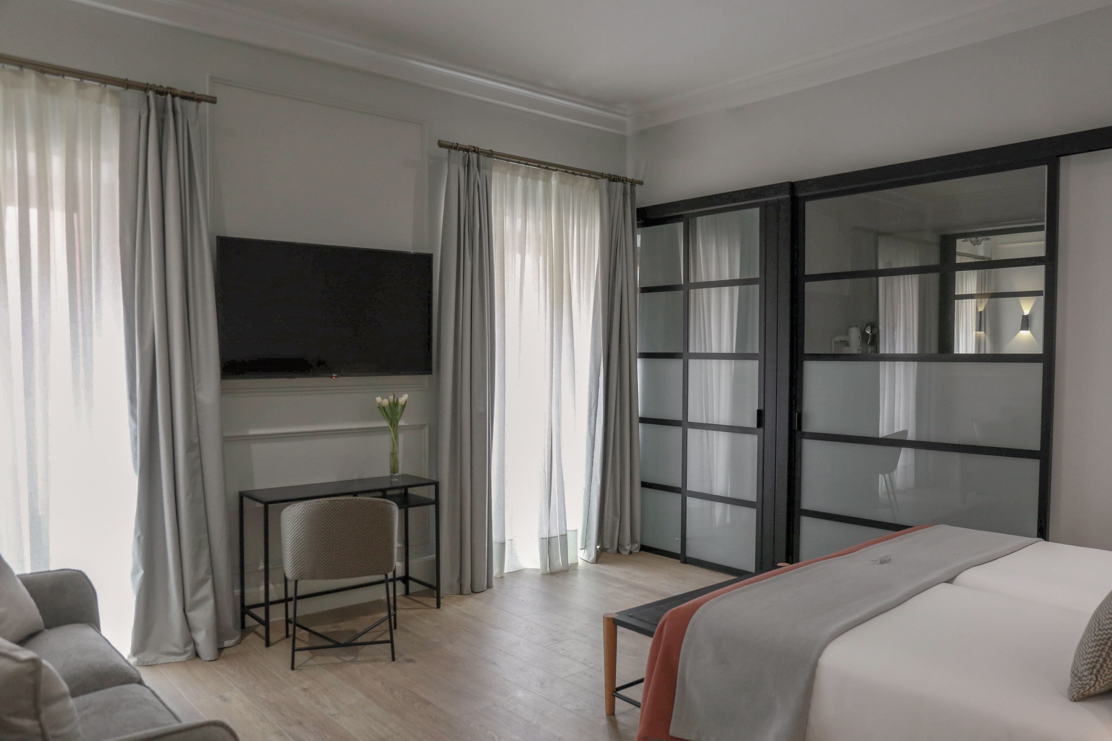 Een hotelkamer met een bed, een bureau met stoel, een televisie en een glazen schuifdeur.