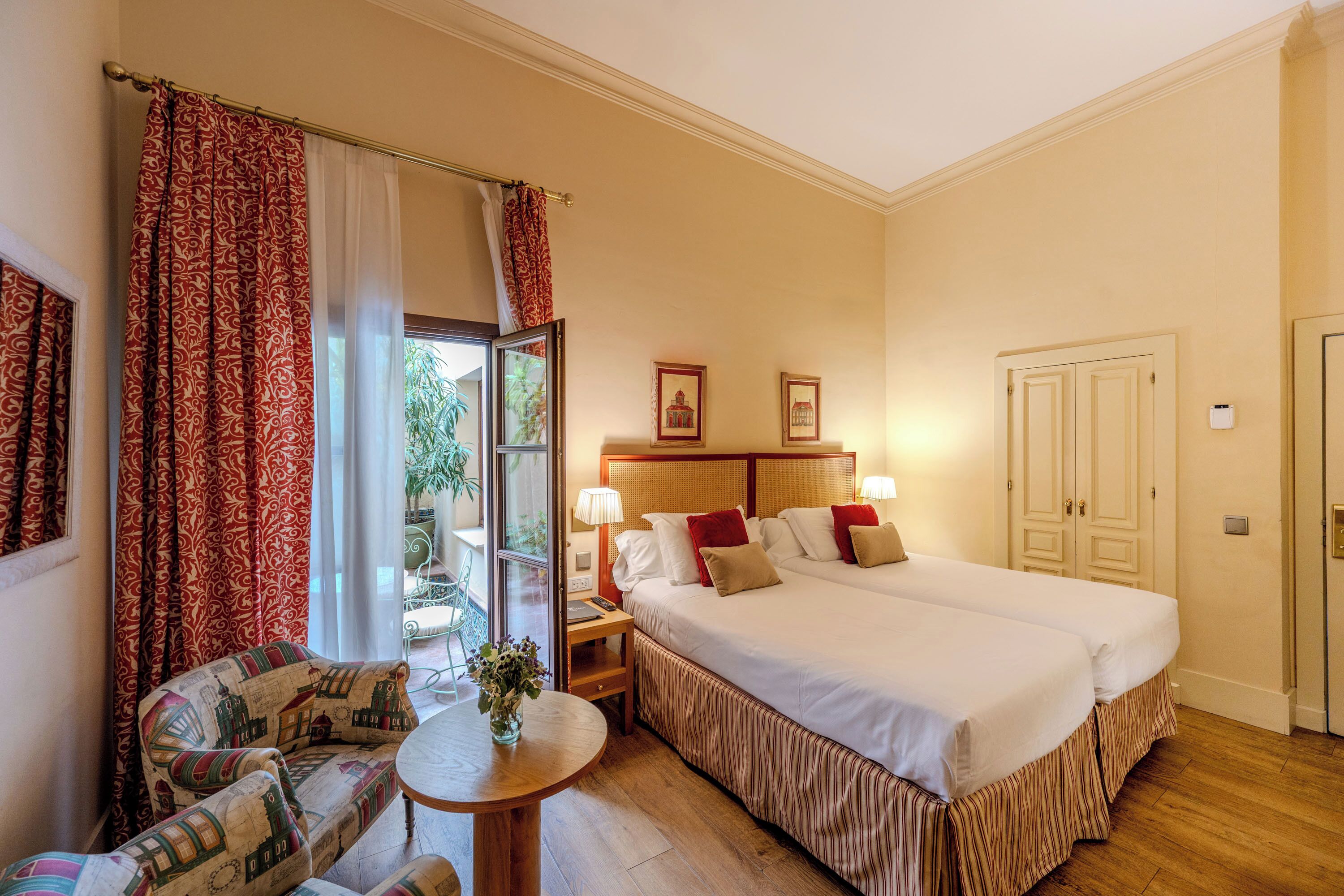 Une chambre d’hôtel avec un grand lit, une petite table sur laquelle est posé un vase, une chaise et une vue sur l’extérieur.