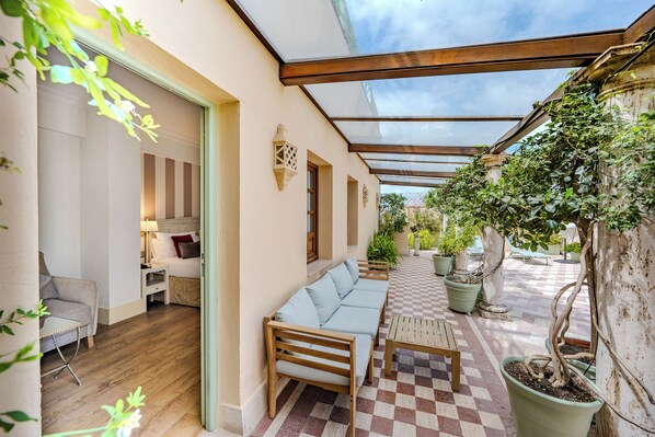 A covered outdoor area with a checkered floor, wooden furniture, and potted plants.