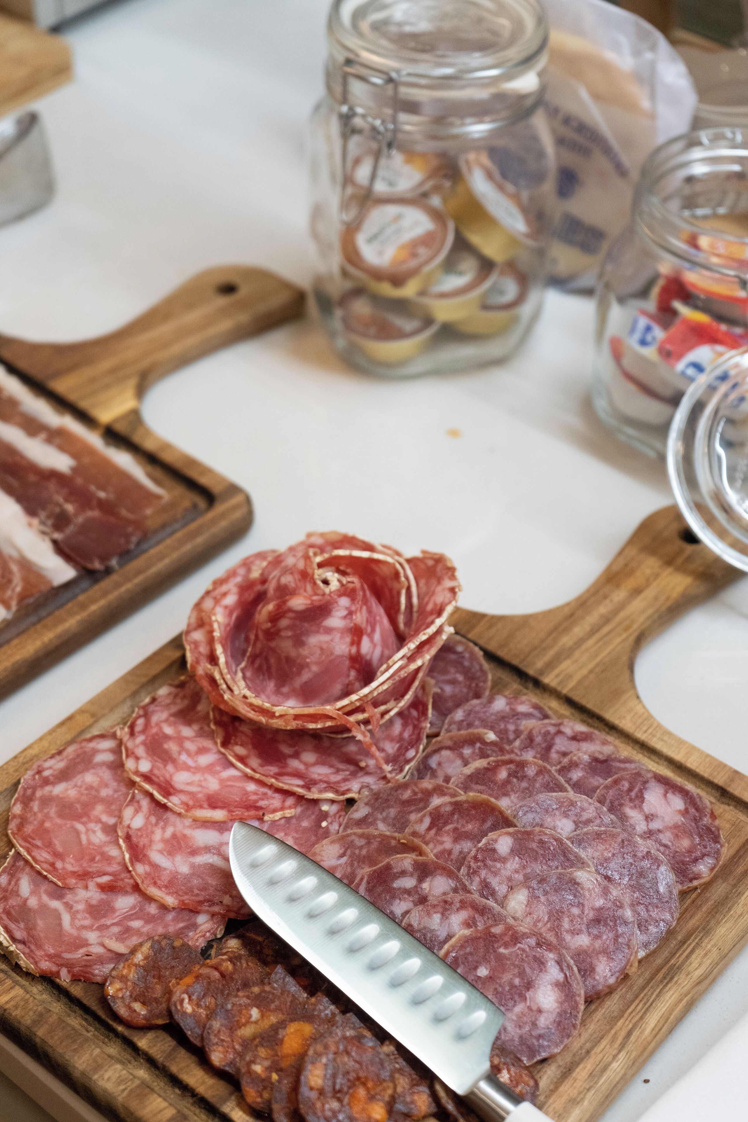 A wooden cutting board with sliced salami and a knife.