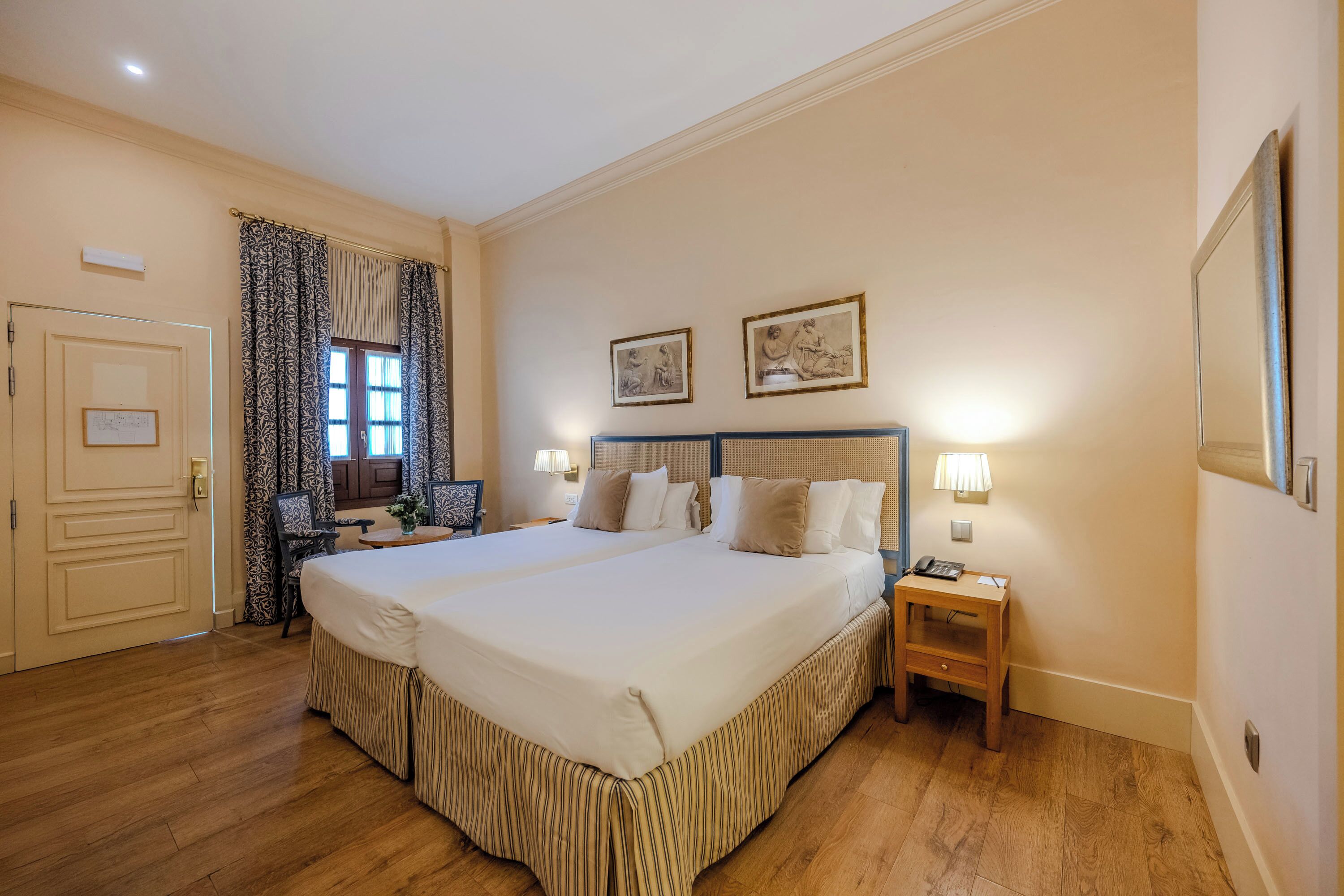 Habitación de hotel con una cama grande, una mesita de noche, un escritorio y dos cuadros en la pared.