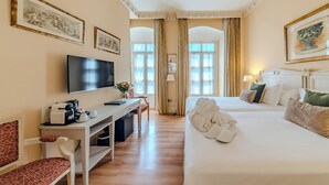 Une chambre d’hôtel équipée d’un lit, d’un bureau, d’une télévision et ornée d’œuvres d’art sur les murs.