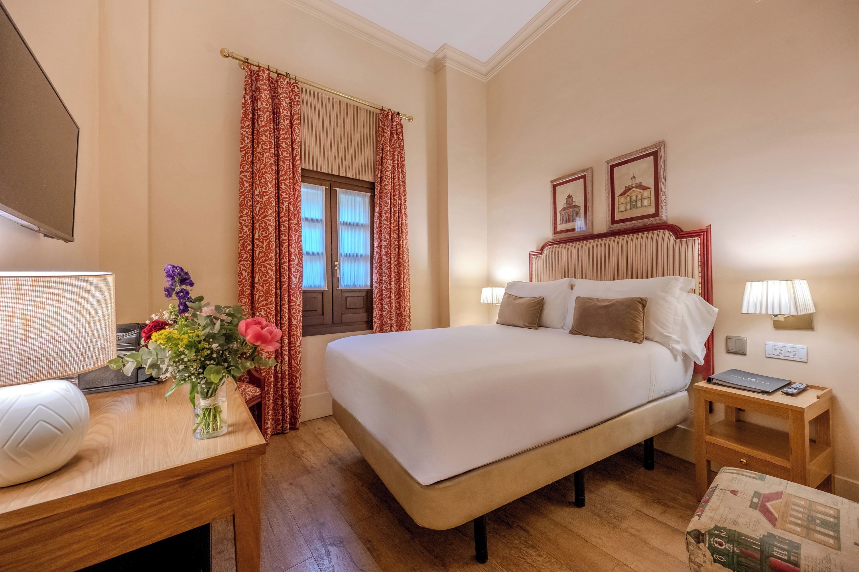Une chambre d’hôtel avec un lit, des tables de chevet, une télévision et une fenêtre avec des rideaux.