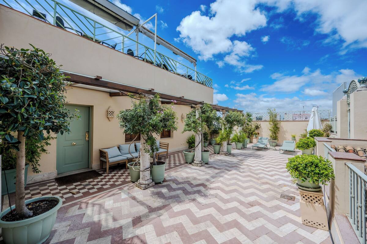 Een dakterras met een zwart-wit betegelde vloer, plantenbakken, terrasmeubilair en een helderblauwe lucht.