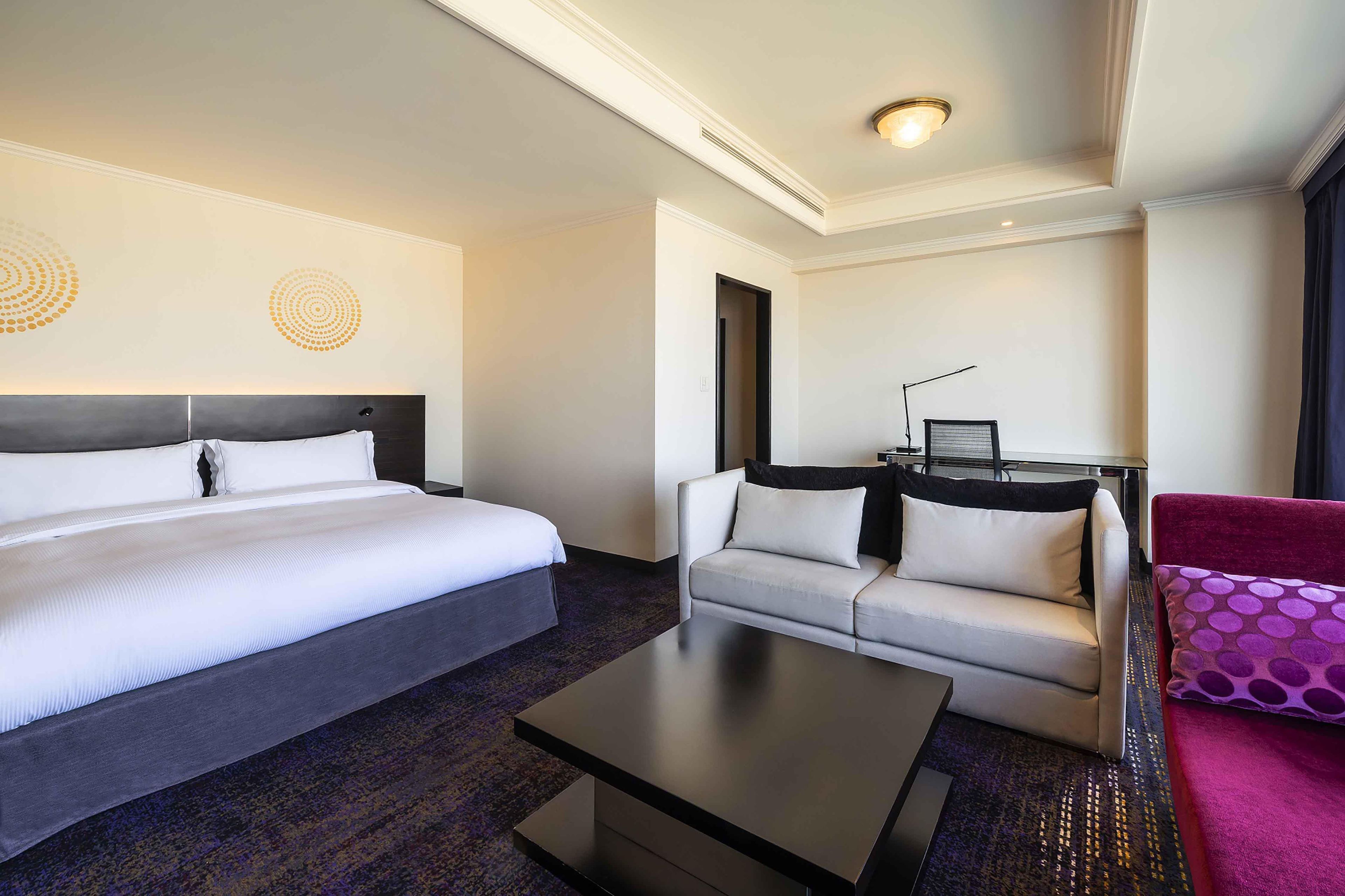 Una habitación de hotel con una cama, un sofá, una mesita de centro y un escritorio con lámpara.
