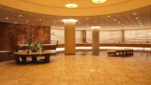 A spacious lobby with a marble floor, a round table with a vase of flowers, and a seating area with benches.
